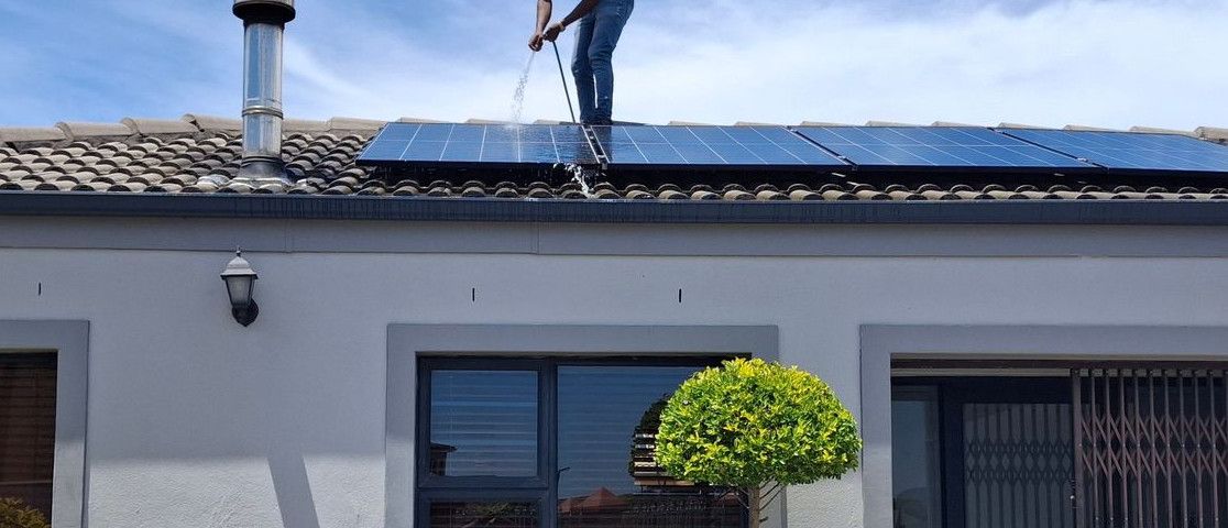 A person maintains solar panels on a house roof under a clear blue sky.